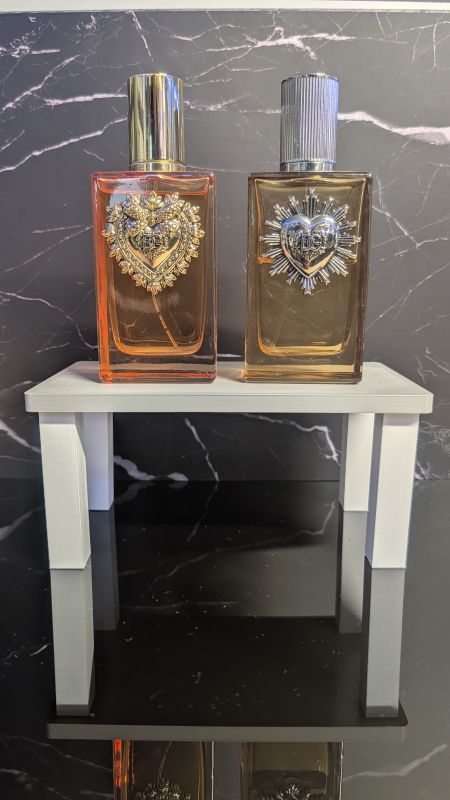 White 3D printed shelf riser holding two perfume bottles above a black marble surface